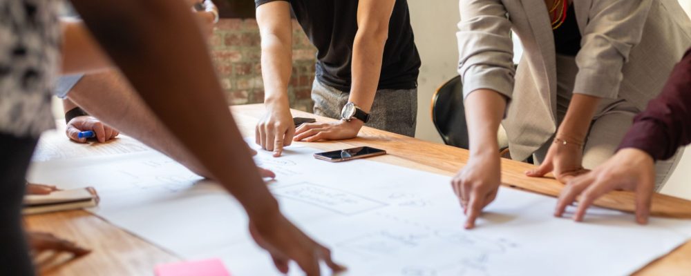Diverse,Group,Of,People,Collaborating,Around,A,Table,,Pointing,At